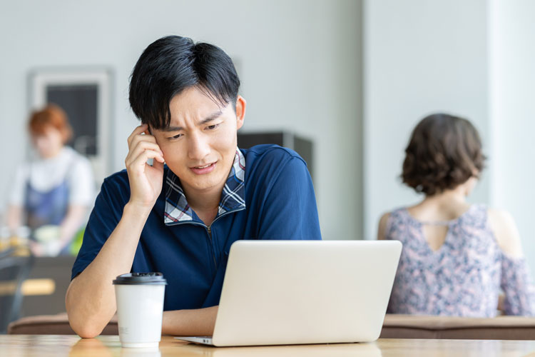 ノートPCの画面を見ながら、こめかみに手を当てる男性